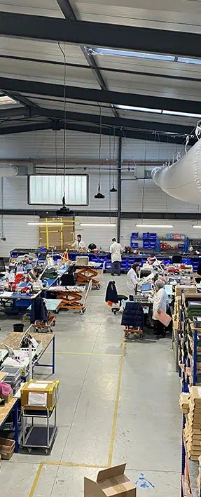 Vue large de l'atelier, des hommes et des femmes en blouses blanches travaillent dans un grand hangar.